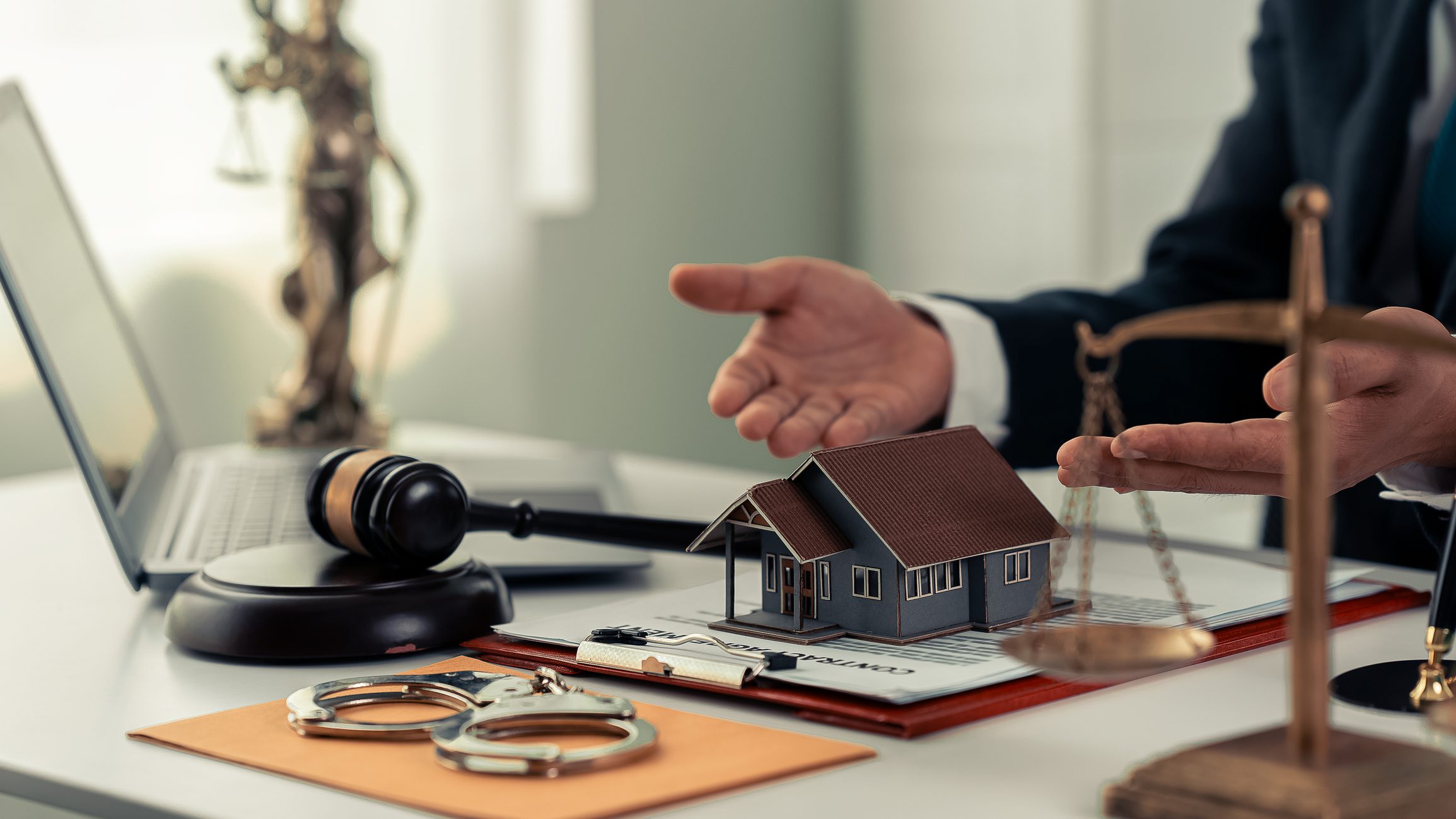 Gavel, house model, scales, and handcuffs on desk.
